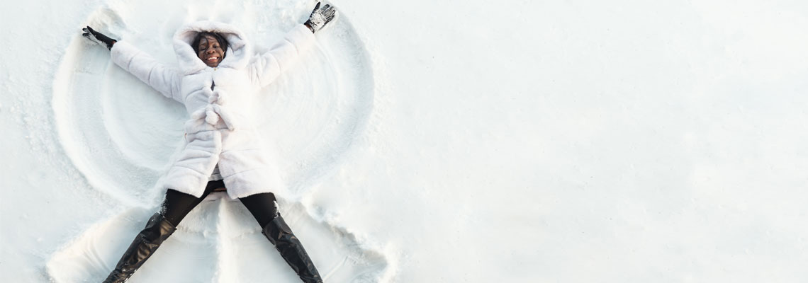 girl in fur coat lies on snow and draws snow angel with arms and legs