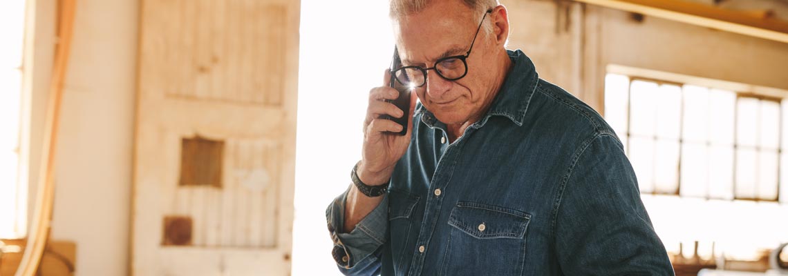 Senior man talking on mobile phone and using laptop on work table