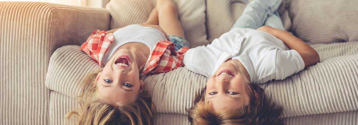 kids lying on their backs on sofa, looking at camera and smiling while playing at home