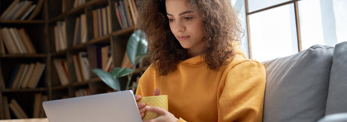 young woman sitting on sofa with pet cat watching webinar on laptop