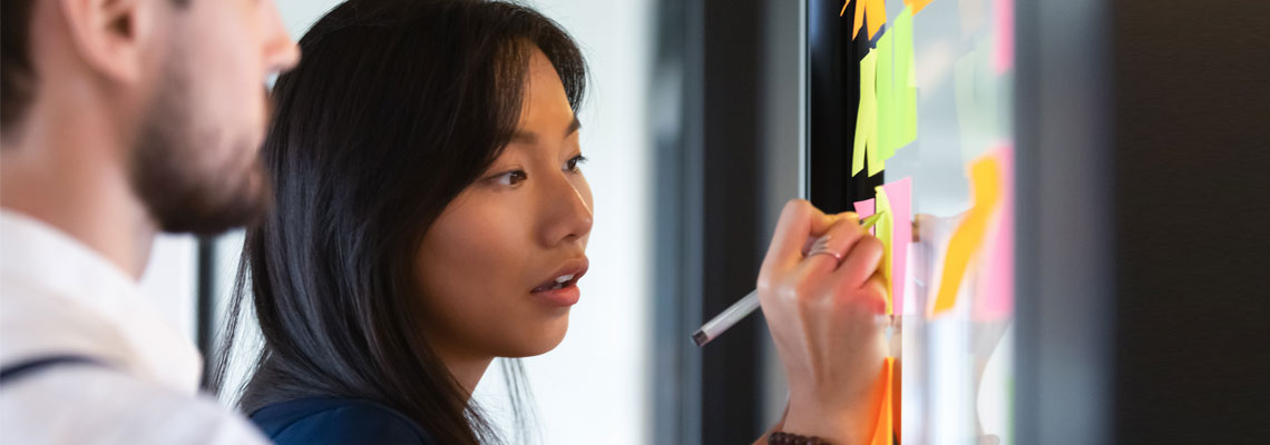 Focused woman writing idea on post it sticky notes on glass wall